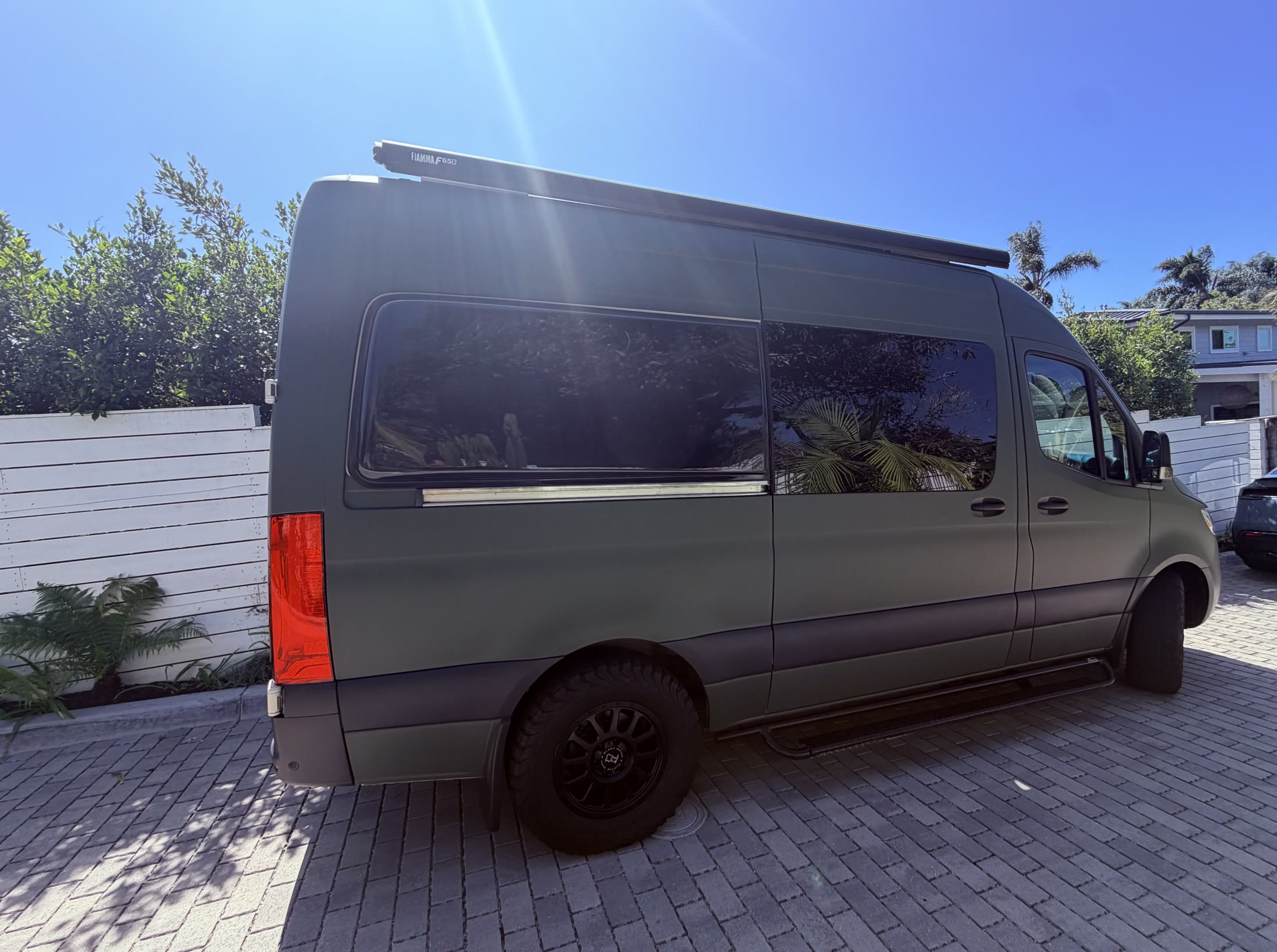 Matte green Mercedes-Benz Sprinter camper with a roof-mounted Fiamma canopy viewed from the passenger side